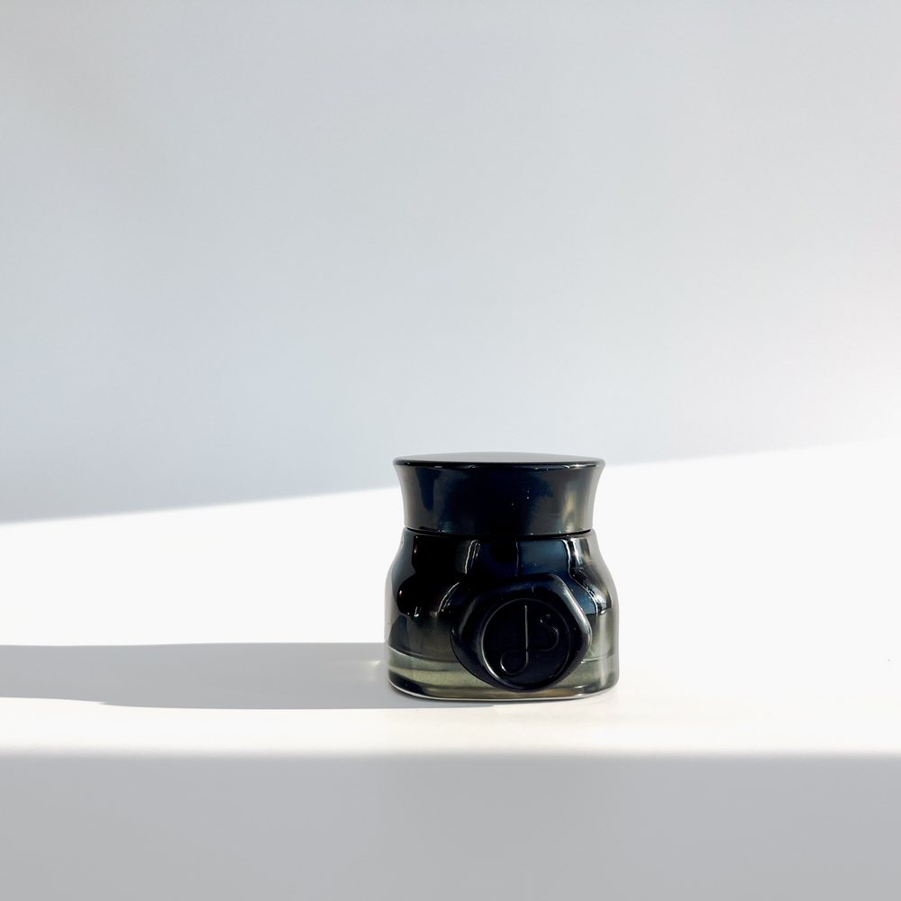 Green black jar on white background filled with skincare cream 